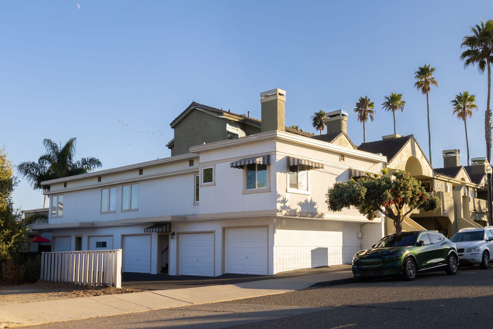 Building One from Ocean View Avenue: white stucco, a deep flat roof line, striped awnings and the upper floor cantilevered over the garages, with palms behind