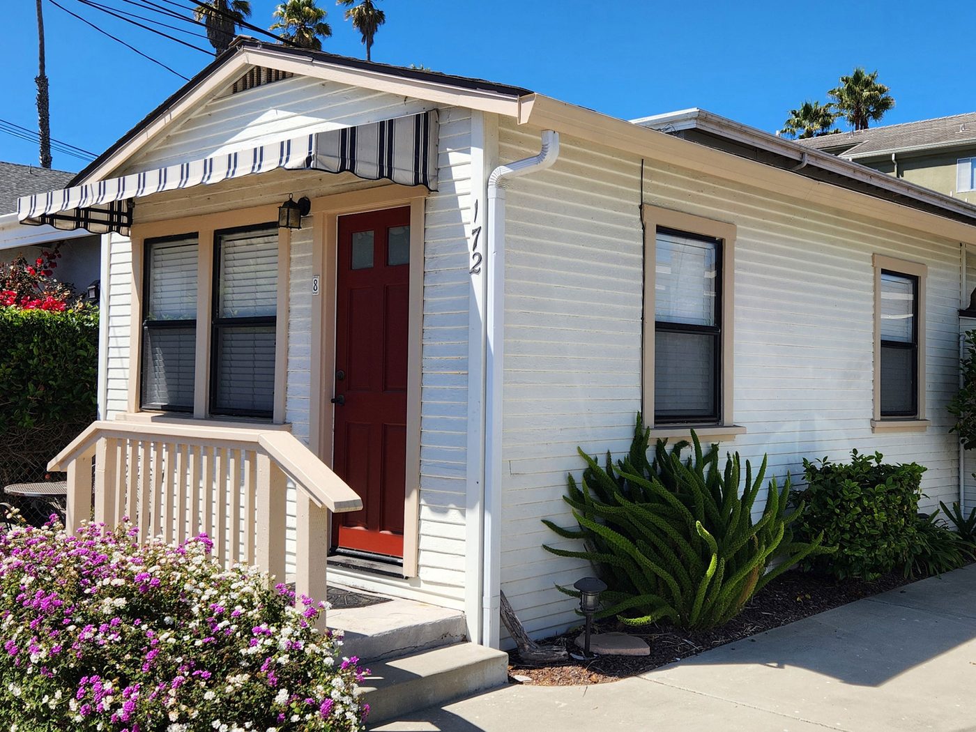 Cottage 8: a detached one-bedroom cottage with a red door, covered stoop and flowering border