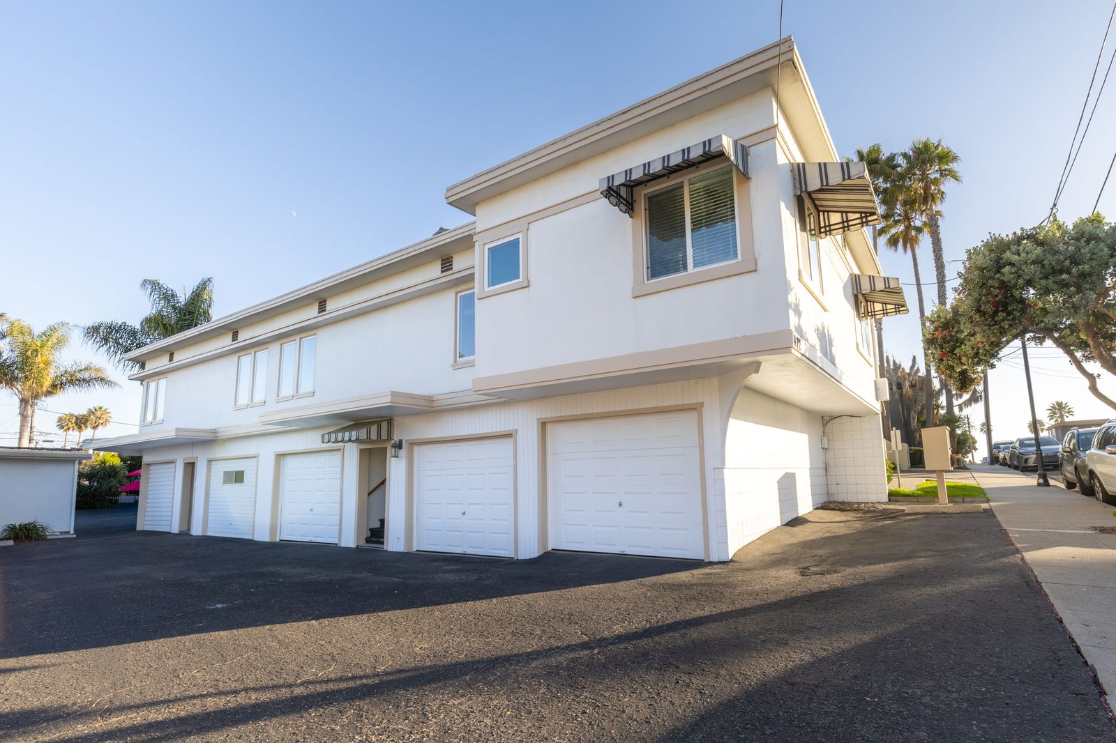 Building One at Pismo Cove Apartments: two upstairs apartments over the garages, with palms behind and the Ocean View Avenue sidewalk at right