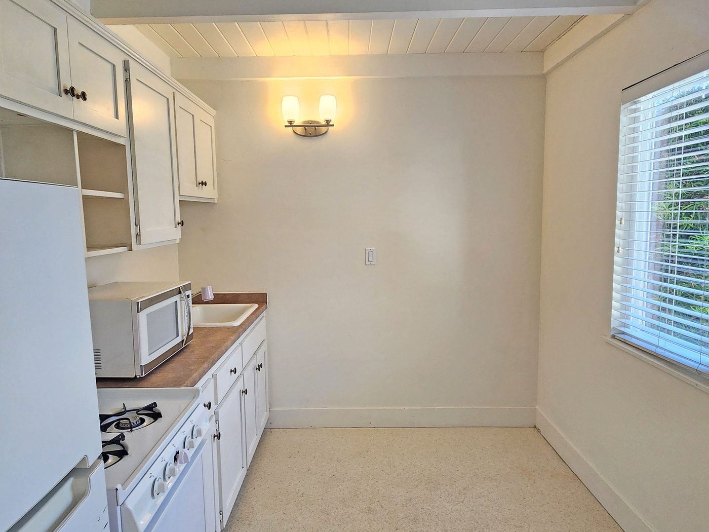 A small white kitchen with a gas range and refrigerator